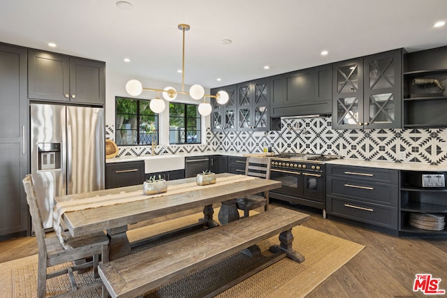 kitchen with decorative backsplash, dark wood-type flooring, stainless steel appliances, an inviting chandelier, and decorative light fixtures