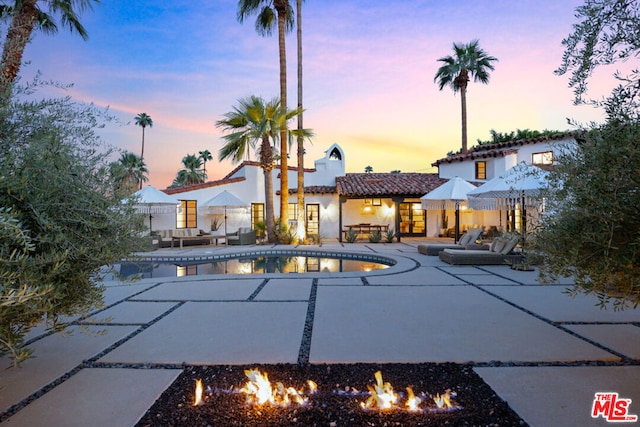 pool at dusk with a patio and a fire pit