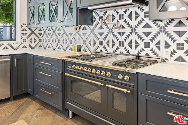 kitchen with appliances with stainless steel finishes, decorative backsplash, light hardwood / wood-style flooring, and exhaust hood