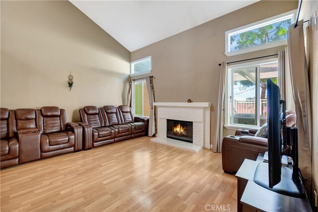 living room with a brick fireplace, light wood-type flooring, and high vaulted ceiling