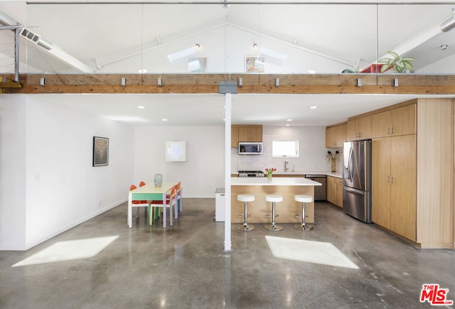 kitchen with backsplash, concrete flooring, stainless steel appliances, lofted ceiling with beams, and a kitchen breakfast bar