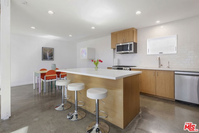 kitchen with appliances with stainless steel finishes, backsplash, concrete floors, and a center island