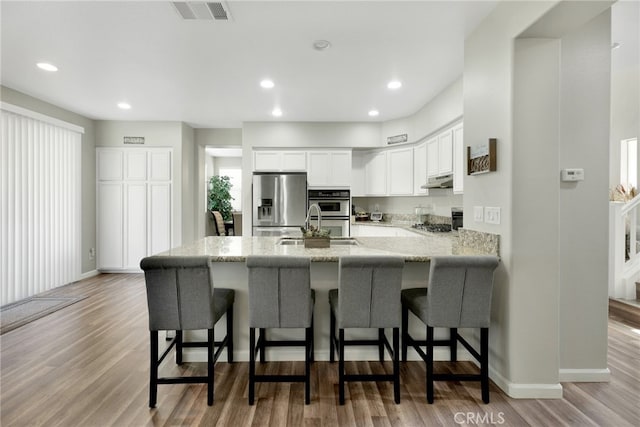 kitchen with white cabinets, light hardwood / wood-style floors, stainless steel appliances, light stone countertops, and a kitchen bar