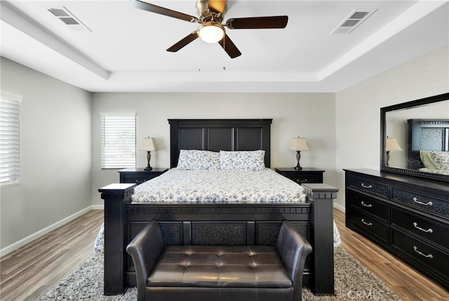 bedroom with light wood-type flooring, a tray ceiling, and ceiling fan