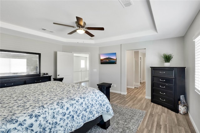 bedroom featuring ceiling fan, light hardwood / wood-style flooring, and a tray ceiling