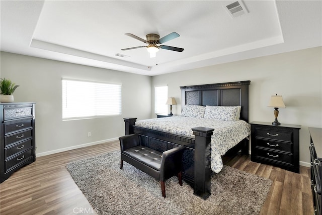 bedroom with ceiling fan, a raised ceiling, and dark hardwood / wood-style floors