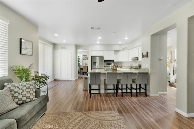 kitchen with white cabinets, kitchen peninsula, light hardwood / wood-style flooring, appliances with stainless steel finishes, and a kitchen breakfast bar