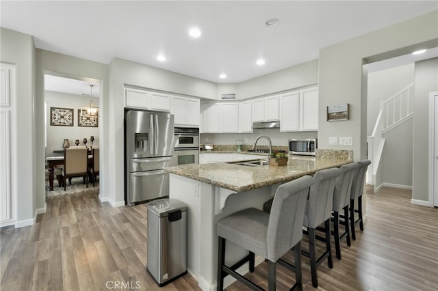 kitchen featuring a notable chandelier, white cabinets, kitchen peninsula, appliances with stainless steel finishes, and hardwood / wood-style floors