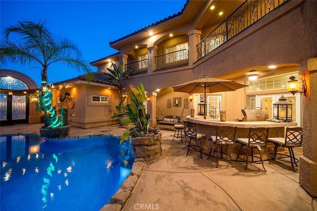 pool at night with exterior bar and a patio