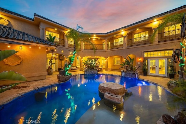 pool at dusk with french doors, a patio, and pool water feature