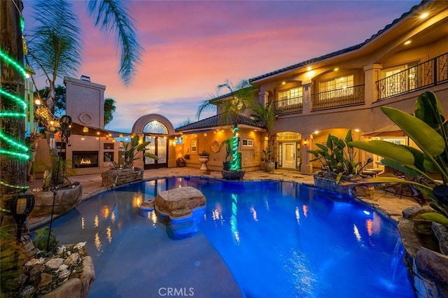 pool at dusk featuring pool water feature and a patio