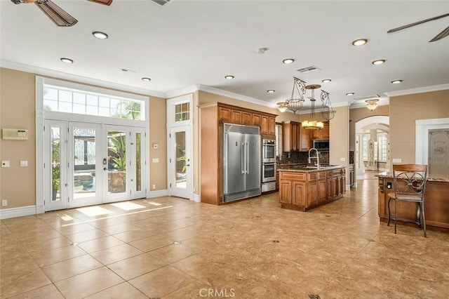 kitchen with a kitchen island with sink, decorative backsplash, ornamental molding, appliances with stainless steel finishes, and decorative light fixtures