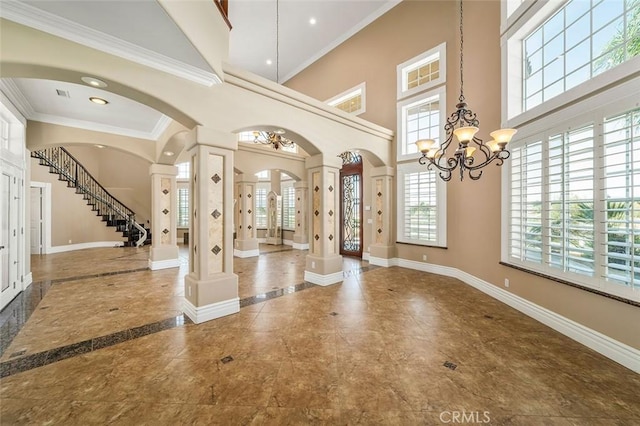 foyer featuring decorative columns, an inviting chandelier, a high ceiling, and ornamental molding