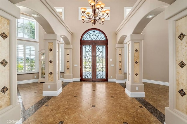 entrance foyer featuring decorative columns, french doors, a towering ceiling, and an inviting chandelier