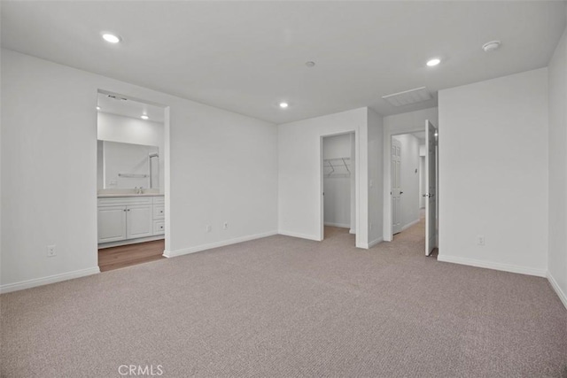 unfurnished bedroom with connected bathroom, a walk in closet, a closet, and light colored carpet