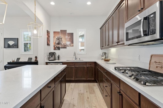 kitchen with appliances with stainless steel finishes, light wood-type flooring, dark brown cabinetry, sink, and decorative light fixtures