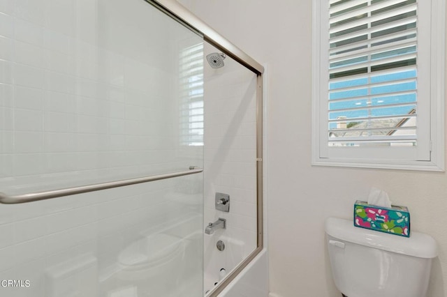 bathroom featuring toilet and bath / shower combo with glass door