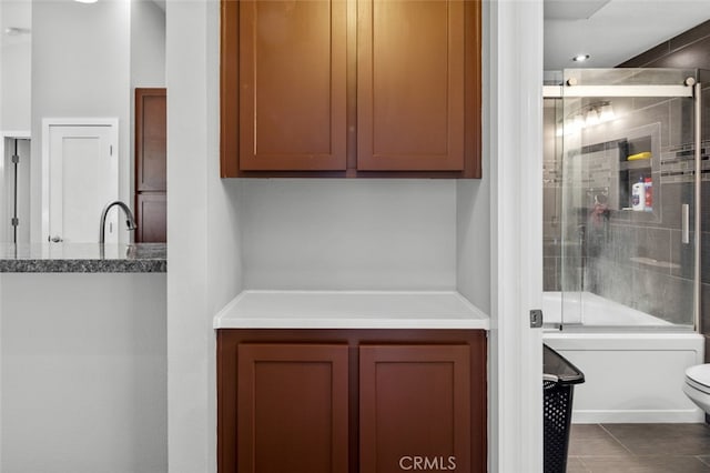 interior details with combined bath / shower with glass door, sink, tile patterned floors, and toilet