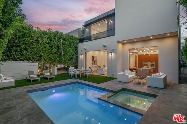 back house at dusk with outdoor lounge area, a pool with hot tub, a balcony, a patio area, and area for grilling