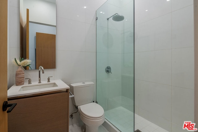 bathroom featuring vanity, toilet, a shower with door, and tile walls