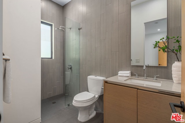 bathroom with tile patterned floors, toilet, tiled shower, vanity, and tile walls