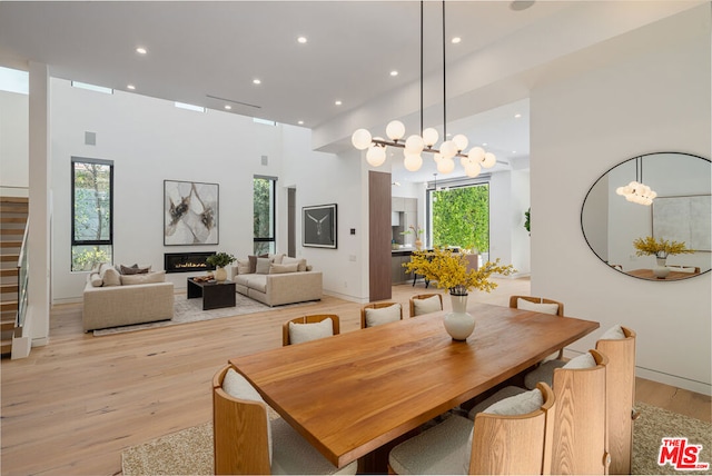 dining space featuring a chandelier, a towering ceiling, a healthy amount of sunlight, and light wood-type flooring