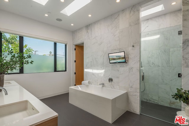 bathroom featuring a skylight, vanity, plus walk in shower, and tile walls