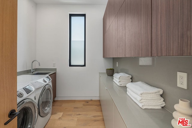 clothes washing area with cabinets, sink, washing machine and dryer, and light hardwood / wood-style flooring