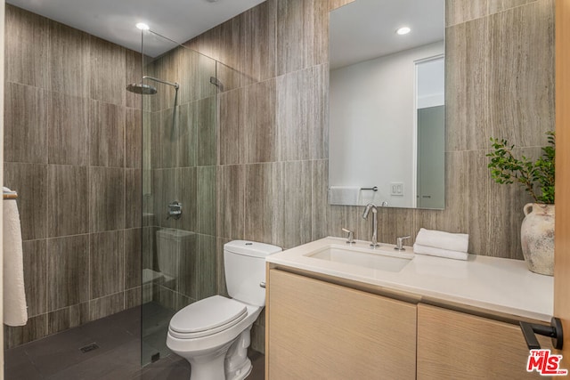 bathroom with a tile shower, vanity, toilet, and tile walls