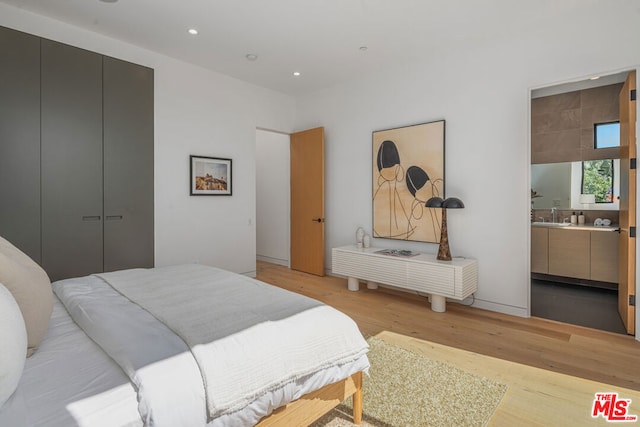 bedroom with ensuite bathroom, light hardwood / wood-style floors, and sink