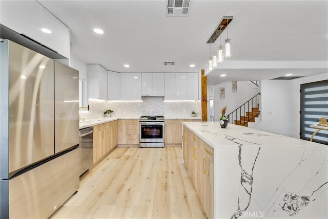 kitchen featuring white cabinets, pendant lighting, light brown cabinets, stainless steel appliances, and light wood-type flooring