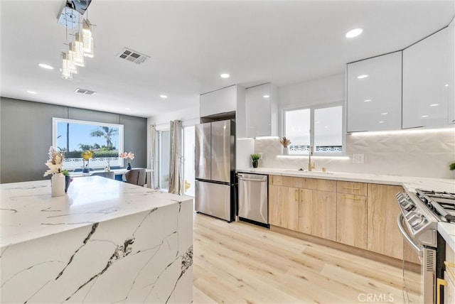 kitchen with white cabinets, light brown cabinets, hanging light fixtures, stainless steel appliances, and light hardwood / wood-style floors