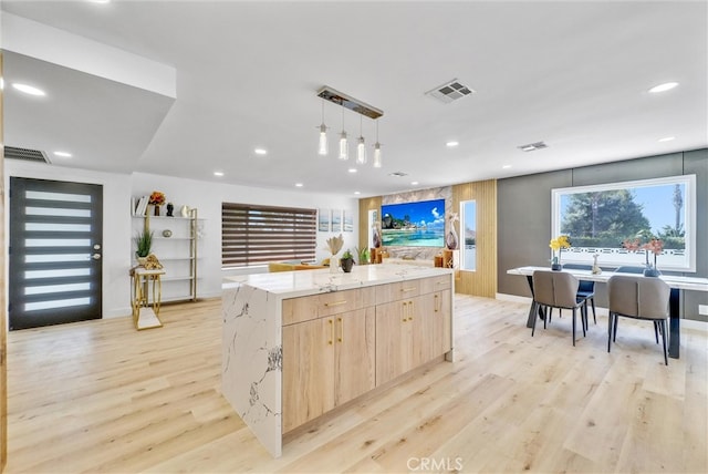 kitchen with a large island, light stone counters, hanging light fixtures, light hardwood / wood-style flooring, and light brown cabinets