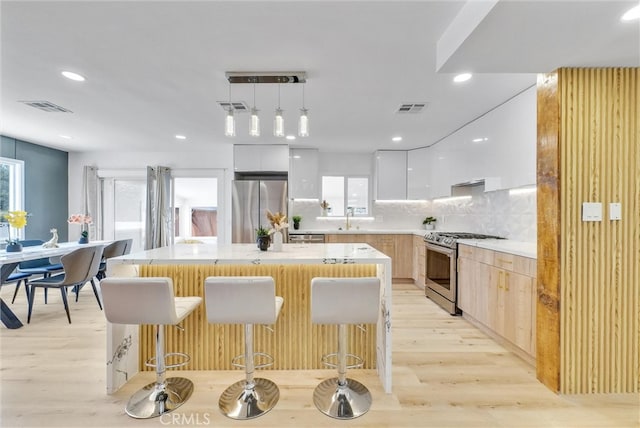 kitchen with pendant lighting, plenty of natural light, white cabinets, a kitchen island, and stainless steel appliances