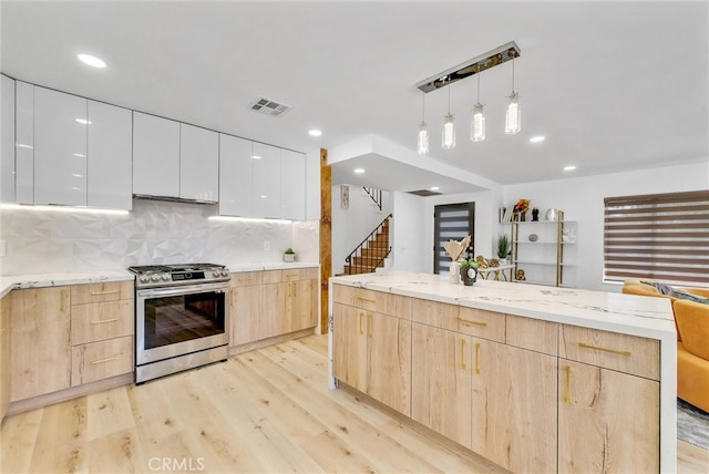 kitchen featuring stainless steel gas range, white cabinetry, light brown cabinetry, and light wood-type flooring