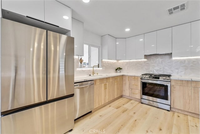 kitchen with appliances with stainless steel finishes, light brown cabinetry, light hardwood / wood-style flooring, and white cabinets