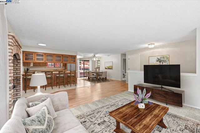 living room with ceiling fan, a textured ceiling, a brick fireplace, and light hardwood / wood-style floors