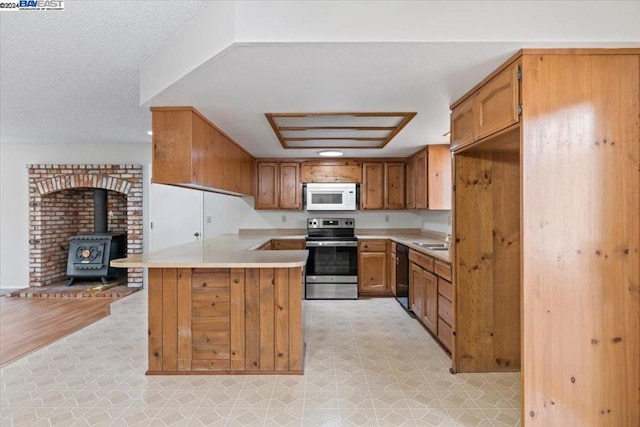 kitchen with dishwasher, sink, stainless steel range with electric cooktop, a wood stove, and kitchen peninsula