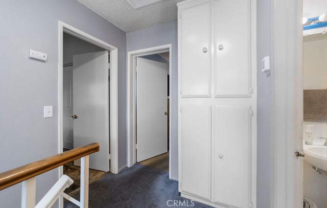 hall featuring dark carpet and a textured ceiling