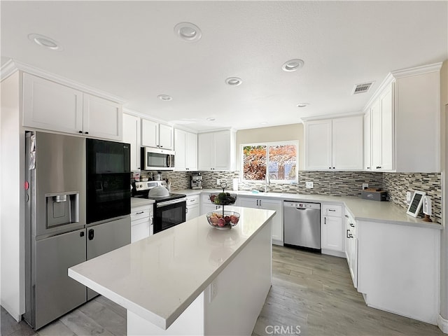 kitchen with stainless steel appliances, white cabinetry, light wood-type flooring, and a kitchen island