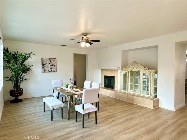 dining area featuring light wood-type flooring, a tiled fireplace, and ceiling fan