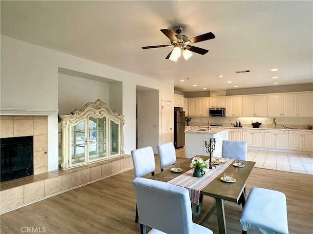 dining area featuring a fireplace, ceiling fan, light hardwood / wood-style flooring, and sink