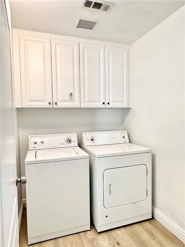 clothes washing area with light wood-type flooring, washer and clothes dryer, and cabinets