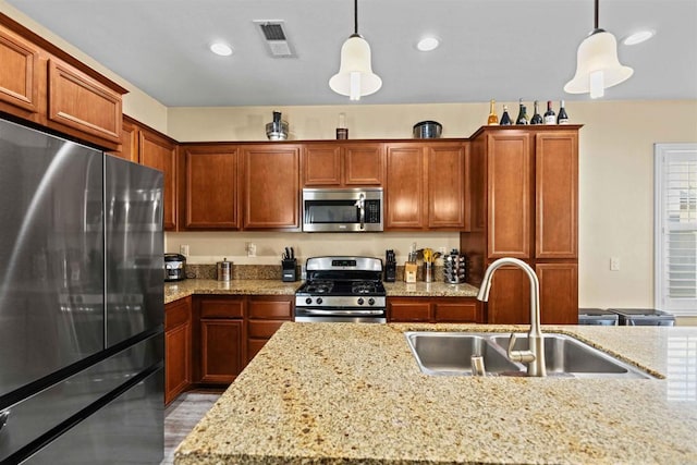 kitchen with light stone countertops, appliances with stainless steel finishes, pendant lighting, and sink