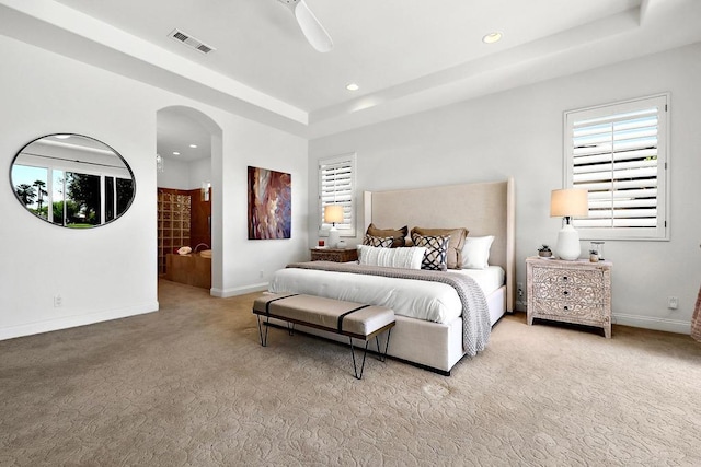 bedroom featuring ceiling fan, a raised ceiling, light carpet, and connected bathroom