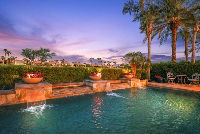 pool at dusk featuring pool water feature