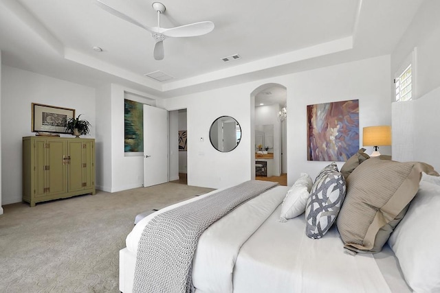 bedroom featuring a tray ceiling, connected bathroom, ceiling fan, and light carpet