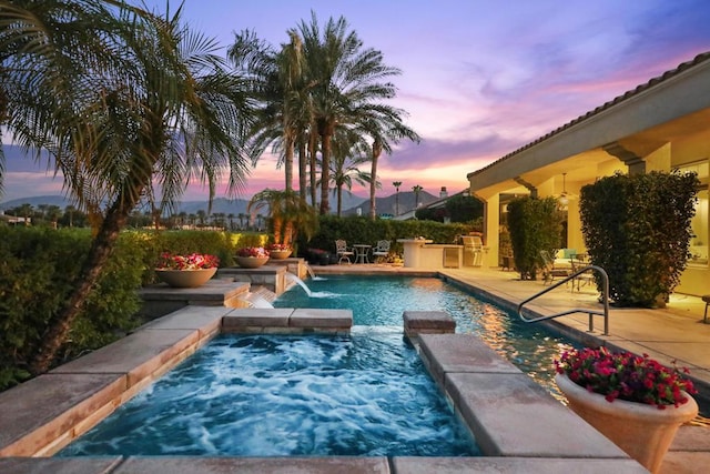 pool at dusk featuring pool water feature, a patio, and a hot tub