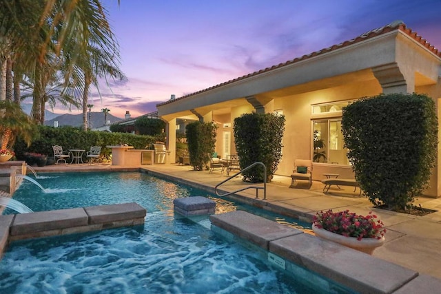 pool at dusk featuring area for grilling, pool water feature, a patio area, and a hot tub