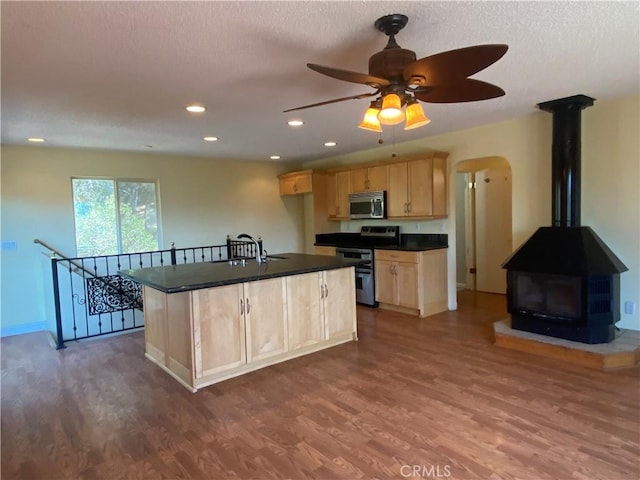 kitchen with light brown cabinets, wood-type flooring, an island with sink, and appliances with stainless steel finishes